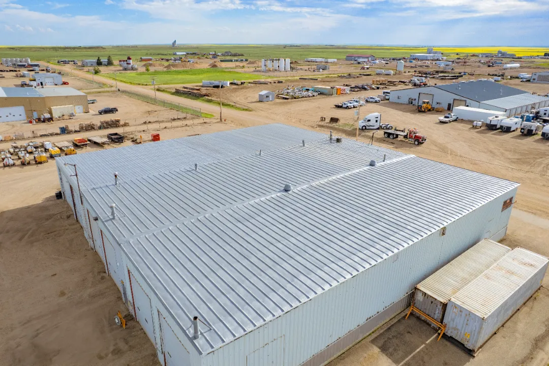 Aerial view of a large industrial building with a metal roof, surrounded by construction equipment and vehicles in a rural area.